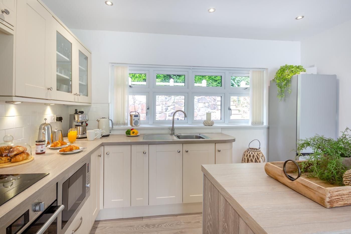 A modern kitchen with white cabinetry, a built-in oven, a sink, and a window with a view of greenery outside.