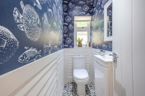 Ein Badezimmer mit Toilette, Waschbecken und Spiegel. Die Wände sind mit einem Fischmuster verziert.