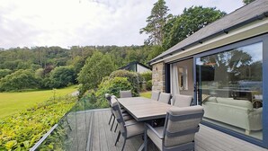 Une terrasse avec une table et des chaises, donnant sur un jardin luxuriant et une colline.