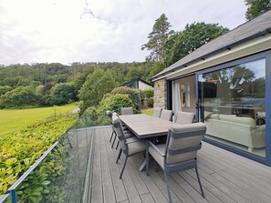 Eine Terrasse mit Tisch und Stühlen mit Blick auf einen üppigen Garten und eine Hügelkette.