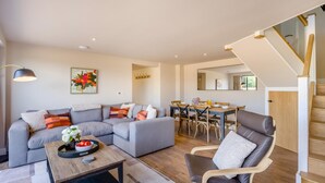 A modern living room with a grey sectional sofa, a wooden dining table, and a staircase with wooden railings. - 2 Bed in Bardwell (oc-d44861) (Bardwell)