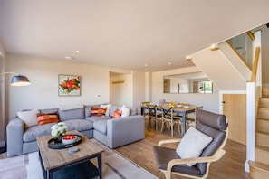 A modern living room with a grey sectional sofa, a wooden dining table, and a staircase with wooden railings. - 2 Bed in Bardwell (oc-d44861) (Bardwell)