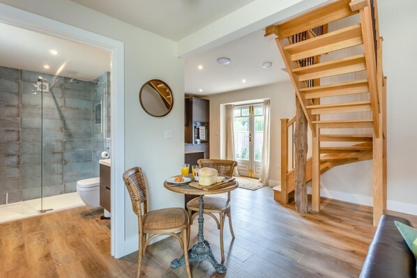 A modern interior with a wooden staircase, a dining area with wicker chairs, and a kitchen in the background.