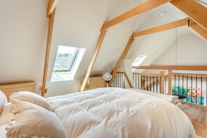 A bedroom with a sloped ceiling, a bed with white bedding, a small bedside table, a fan, and a window with a view of greenery.