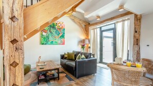 Un salon moderne avec un escalier en bois, un ensemble de canapés, une table basse et un fauteuil en osier.