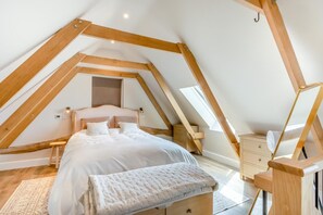 A bedroom with a sloped ceiling, a bed with white bedding, a bedside table, a lamp, and a small wooden cabinet. - 1 Bed in Bardwell (oc-l44860) (Bardwell)