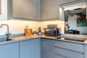 A modern kitchen with grey cabinets, a stainless steel sink, a coffee machine, and a microwave.