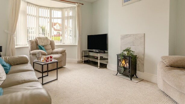 Una sala de estar con sofá, sillón, televisión, chimenea y ventana con cortinas.