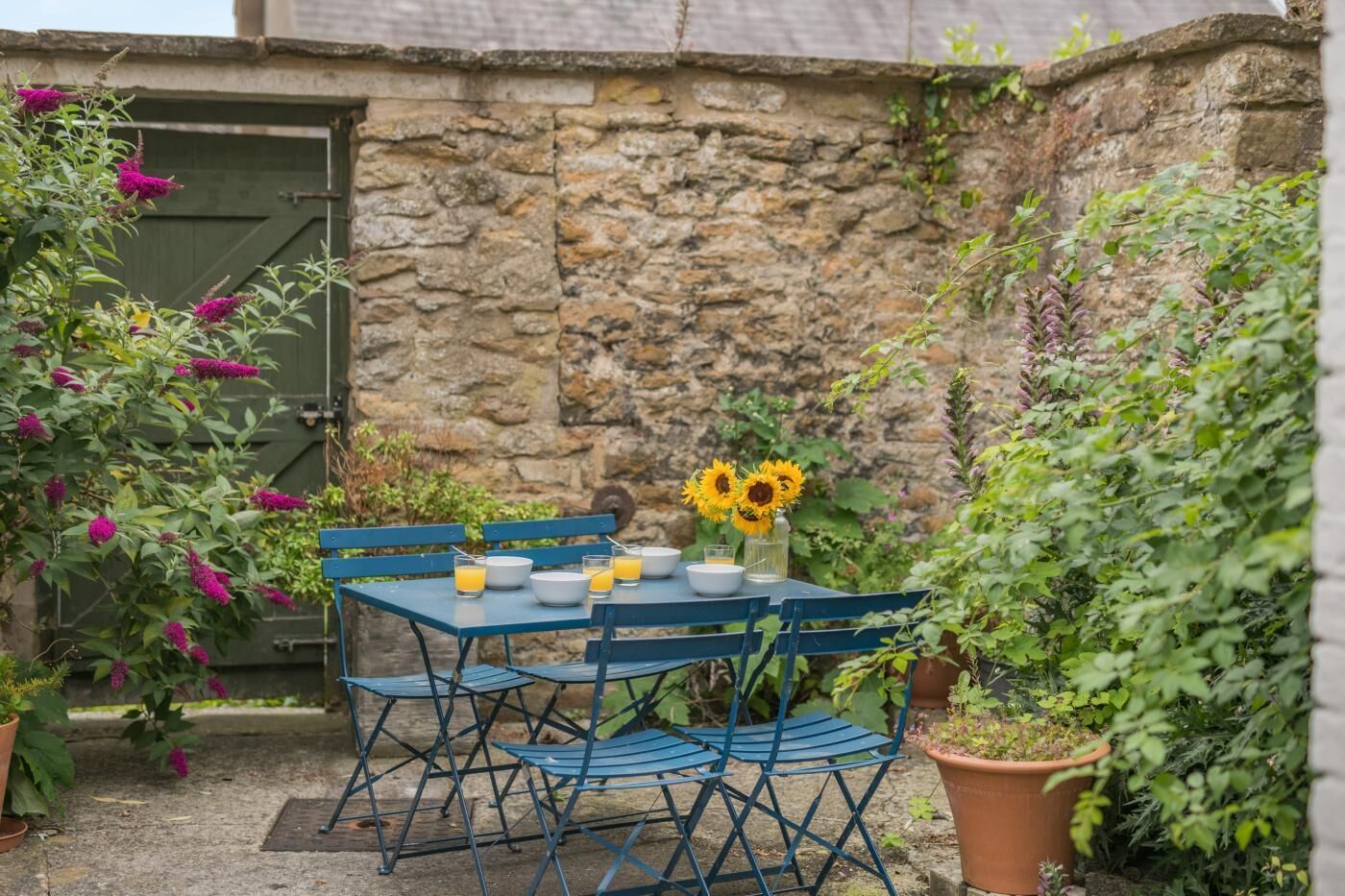 A stone wall with a metal table and chairs, surrounded by potted plants and flowers.