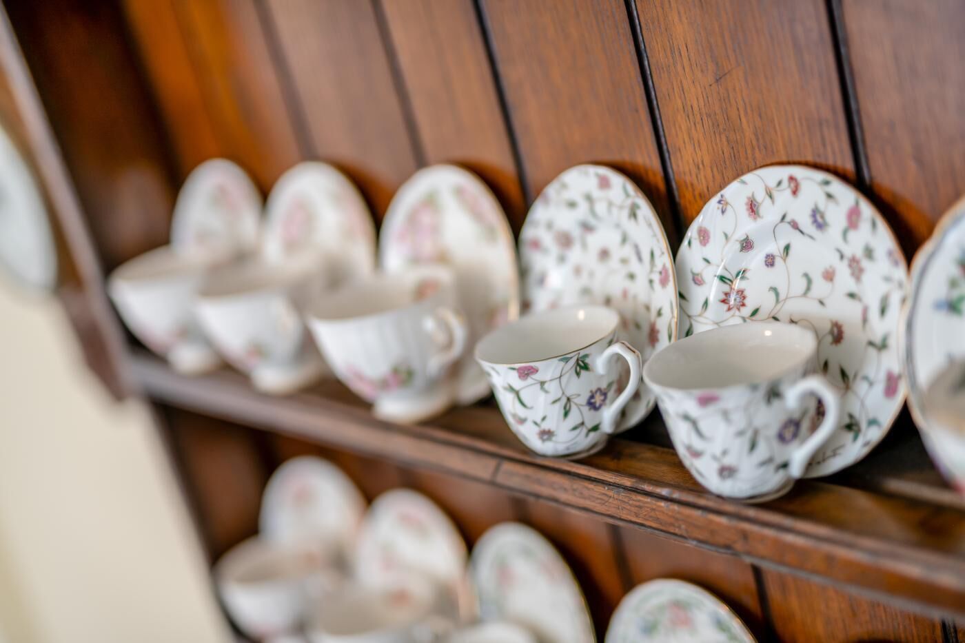 Een houten plank met een verzameling witte keramische kopjes en schotels met bloemenmotieven.