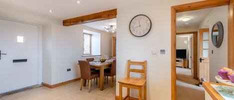 Una habitación amplia con zona de comedor, una silla de madera y un reloj de pared.