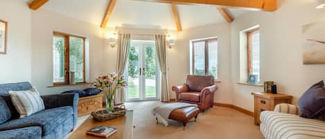 A spacious living room with a high ceiling, a fireplace, and a view of the outdoors through large windows.