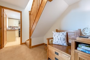 A bedroom with a wooden bed, a bedside table with books, a wall clock, and a view of a kitchen and bathroom through an open door. - 2 Bed in Sawdon (oc-w45349) (Sawdon)