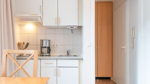 Eine kleine Küche mit weißen Schränken, einer Kaffeemaschine und einem Holzbstuhl.