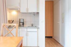 Ett kompakt kök med vita skåp, en kaffebryggare och en trästol.