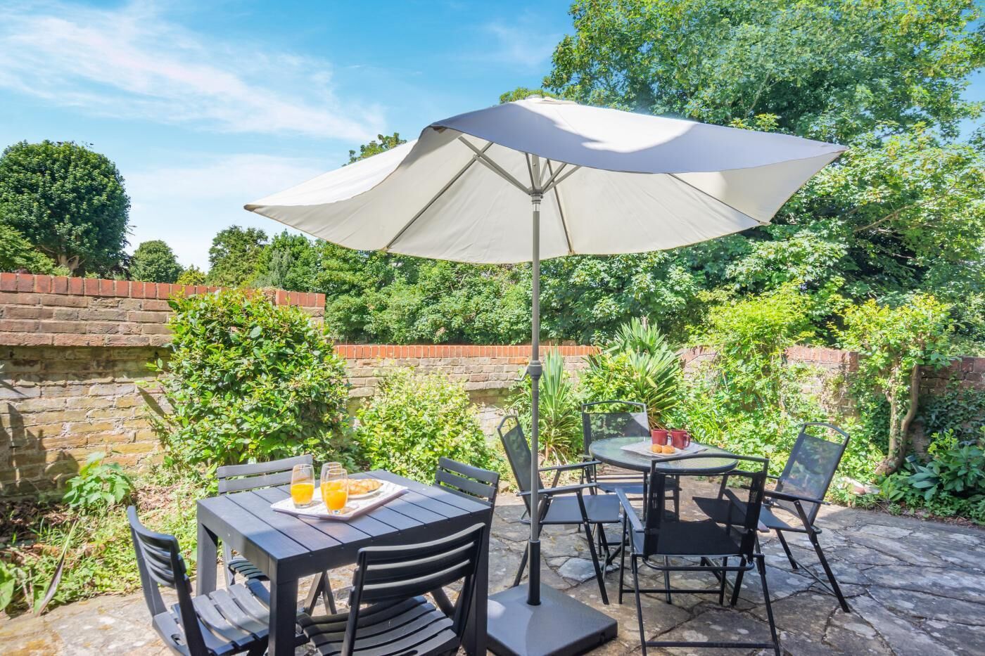 Eine Terrasse im Freien mit Tischen, Stühlen und einem großen Sonnenschirm, an einer Backsteinmauer.