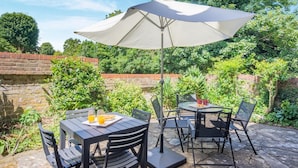 En udendørs patio med borde og stole, en stor parasol og en murstensvæg.