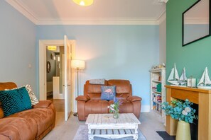 A living room with a brown leather sofa, a wooden coffee table, and a bookshelf with model ships. - 2 Bed in Eastbourne (oc-e44809) (Eastbourne)