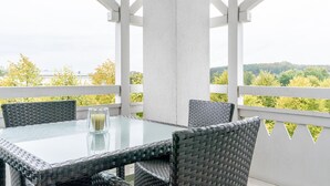 A covered outdoor seating area with a glass table and wicker chairs, overlooking a green landscape. - Schone Ferienwohnung mit Wanne und Grossem Balkon in Sellin (Sellin)