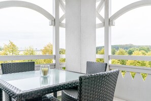 A covered outdoor seating area with a glass table and wicker chairs, overlooking a green landscape. - Schone Ferienwohnung mit Wanne und Grossem Balkon in Sellin (Sellin)