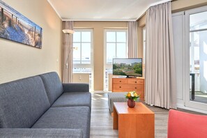 A modern living room with a grey sofa, a wooden coffee table with a vase, a flat-screen TV, and a large window with curtains. - Schone Ferienwohnung mit Wanne und Grossem Balkon in Sellin (Sellin)