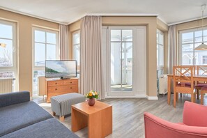 A modern living room with a sofa, ottoman, wooden coffee table, TV, and dining area with chairs and a table. - Schone Ferienwohnung mit Wanne und Grossem Balkon in Sellin (Sellin)
