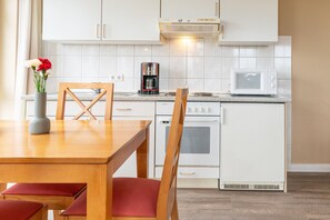 A compact kitchen with white cabinets, a microwave, a coffee maker, and a dining table with chairs. - Schone Ferienwohnung mit Wanne und Grossem Balkon in Sellin (Sellin)