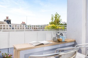 A balcony with a wooden table, a metal chair, a potted plant, and a white fence. - 4 Bed in Brixham (oc-s45328) (Brixham)