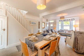 Ein Essbereich mit einem Holztisch, gedeckt für vier Personen, eine Treppe und ein Wohnzimmer mit Sofa und Lampe.