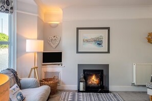 A cozy living room with a fireplace, a flat-screen TV, and a framed painting above it. - 4 Bed in Brixham (oc-s45328) (Brixham)
