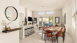 A modern kitchen with a bar area, dining space with orange chairs, and a large mirror. - Your Own Private Luxe Brand New Resort (Bermuda Dunes)
