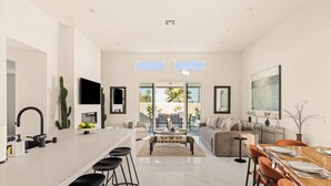 A modern kitchen with a central island, bar stools, a dining area with a wooden table, and a living room with a sofa and coffee table. - Your Own Private Luxe Brand New Resort (Bermuda Dunes)