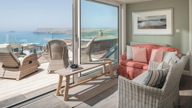 Un balcone con mobili in vimini, un divano rosso con motivi decorativi e un quadro appeso al muro.