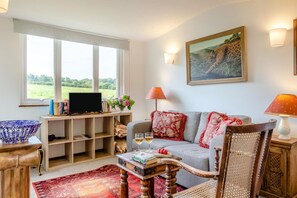 A living room with a sofa, a television, a bookshelf, and a painting on the wall. - 1 Bed in Tawstock (oc-s45343) (Tawstock)
