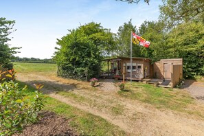 A small wooden cabin with a porch, surrounded by a fenced area and a flagpole with a flag. - 1 Bed in Tawstock (oc-s45343) (Tawstock)