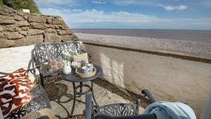 A seaside patio with a table set for two, featuring a vase with flowers, a tray with cups, and a patterned cushion. - 3 Bed in Budleigh Salterton (oc-a44975) (Budleigh Salterton)