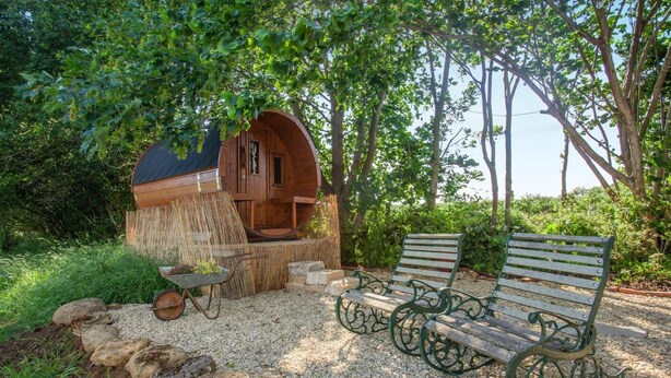 Uma cabana de madeira rústica com um banco e um carrinho de mão num jardim.