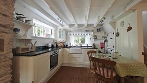 Una cocina con armarios blancos, una mesa de comedor con sillas y una ventana con cortinas.