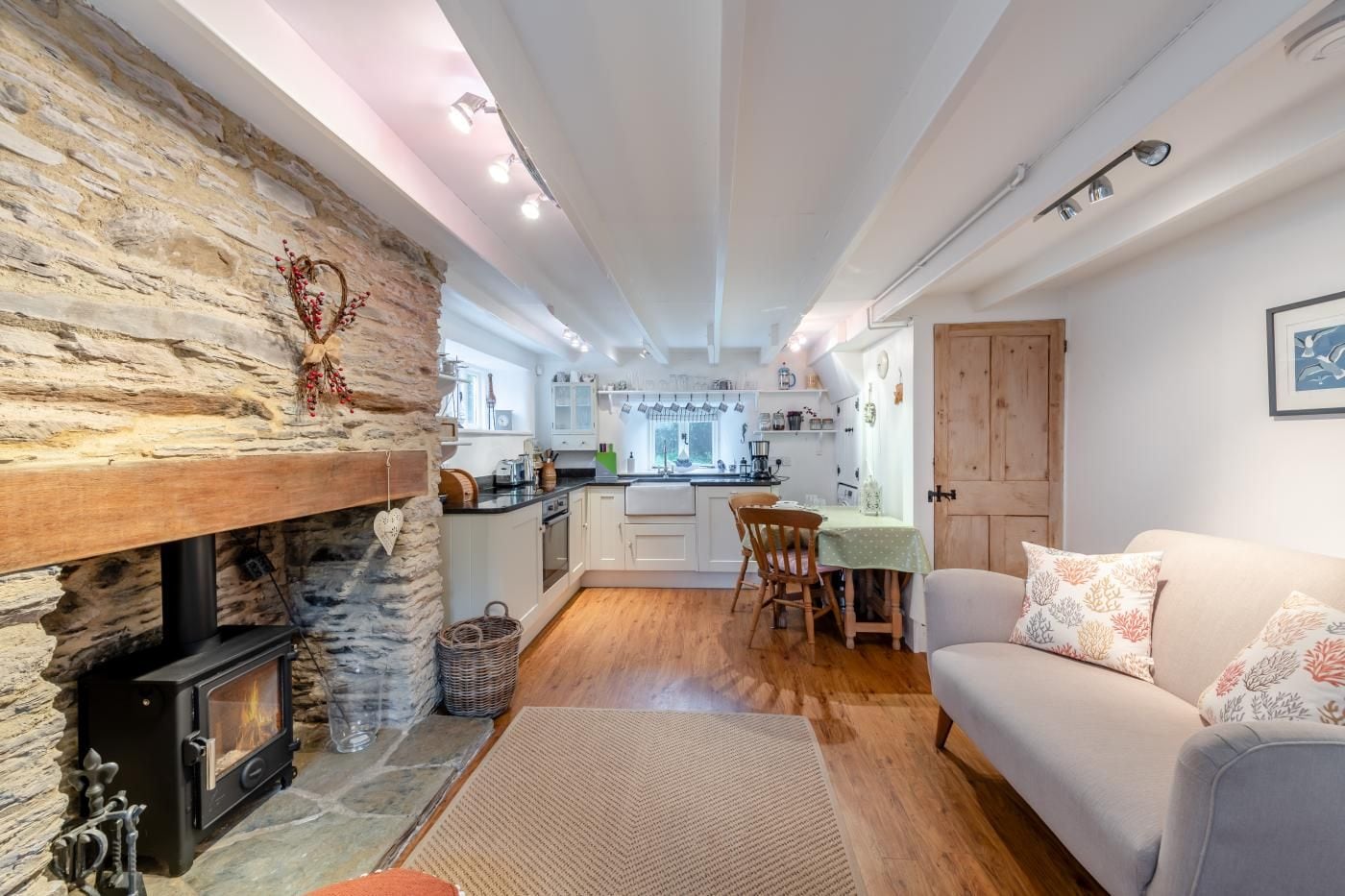 A cozy living room with a stone fireplace, a dining area, and a kitchen with white cabinets and a wooden door.