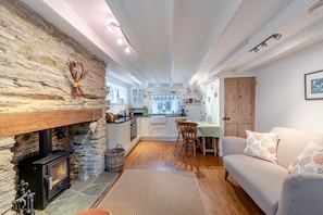 A cozy living room with a stone fireplace, a dining area, and a kitchen with white cabinets and a wooden door. - 2 Bed in Kingston (oc-s43307) (Kingston)