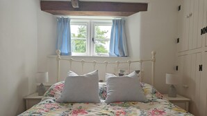Un dormitorio con cama, dos lámparas de noche, una ventana con cortinas y una viga de techo de madera.