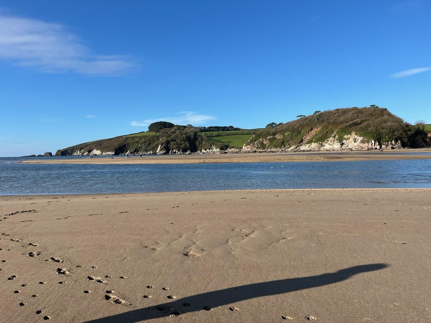A beach with footprints in the sand, a clear sky, and a hill in the background.