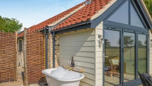 A bathroom with a freestanding bathtub, a glass-enclosed shower, and a window overlooking a garden. - 1 Bed in Bedingham (oc-h44947) (Bedingham)
