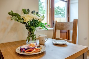 A dining table with a plate of pastries, a vase with flowers, and a mug.