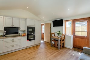 A compact kitchen with white cabinets, a microwave, and an oven. There's a dining area with a table and chairs, and a TV mounted on the wall.