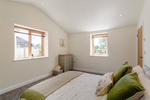 A bedroom with a large bed, two windows, a dresser, and a small plant.