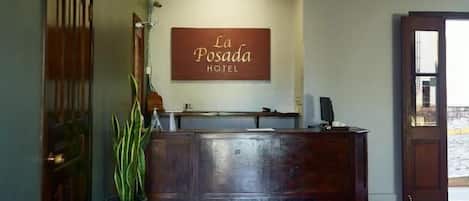 A reception desk with a sign reading 'La Posada Hotel,' a potted plant, and a tiled floor.