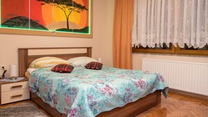 A bedroom with a bed, a nightstand, a window with curtains, and a wall-mounted painting.