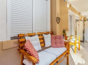 Eine Holzbank mit weißen Kissen und einem roten Kissen mit Punkten, ein kleiner Tisch mit Stühlen und eine herzförmige Dekoration an der Wand.