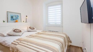 A bedroom with two beds, a TV, a window with blinds, and a framed picture on the wall. - Two Bedroom Apartment near Centar (Rijeka)